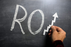 Man holding success arrow over the letters RO written with chalk on blackboard to make the word ROI (Return on Investment)