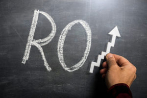 A Recent Report Shows an Impressive Return on Investment for Cabinet Refacing Man holding success arrow over the letters RO written with chalk on blackboard to make the word ROI (Return on Investment)