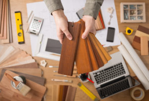 Professional interior designer holding wood swatches for baseboard and skirting, hands close up with desktop on background