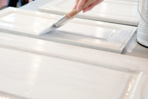 Close up of hand painting kitchen cabinets white.