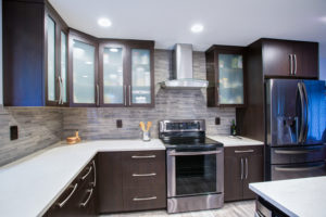 Updated contemporary kitchen room interior with white counters and dark wood cabinets fitted with luxury stainless steel appliances.