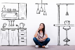 Cheerful young woman smiling while sitting on the floor against white background with drawn kitchen