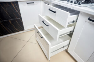 Which Are Better: Cabinet Rollout Trays or Cabinet Drawers? Solution for placing kitchen utensils in modern kitchen - horizontal sliding pullout drawer shelves storage in cupboard for kitchenware cookware under oak countertop gas hob, with copyspace.