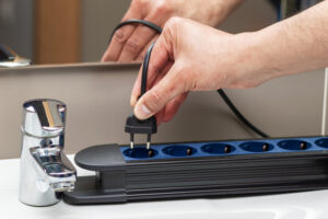 Close up of a man hand plugging electric plug a in a socket at bathroom