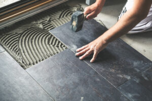 Worker carefully placing ceramic floor tiles on adhesive surface