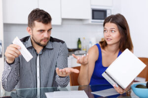 Upset young couple with financial bills and box having conflict at home